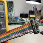 Close-up view of a ribbon cable and multimeter testing for continuity